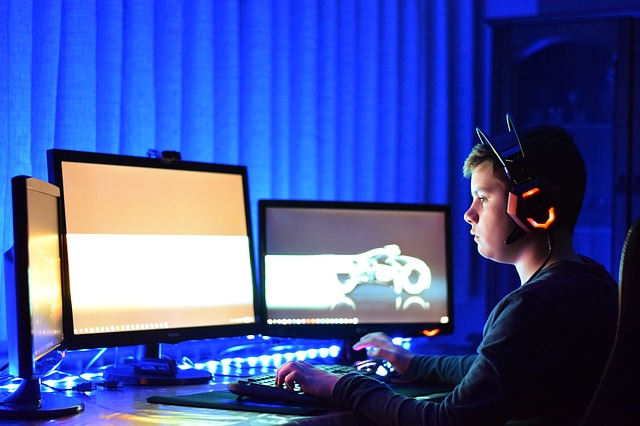 boy sitting in front of 2 computer screens playing online games