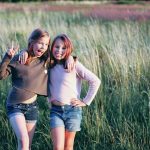 2 teenage girls smiling to camera with arms round each other