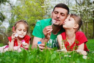 Dad with 2 daughters lying on grass blowing bubbles