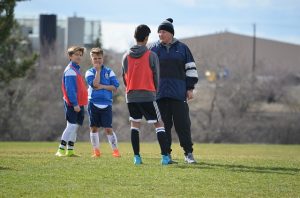 Boy talking to football coach. 2 other boys looking nervous in background.