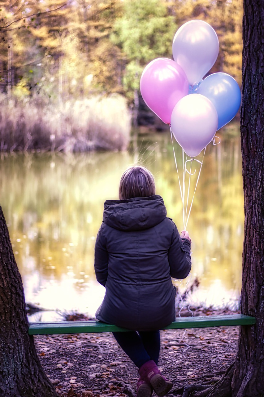 woman sitting alone on bench with a bunch of ballooons