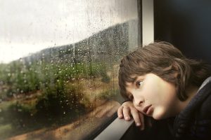 Little boy looking bored - staring out of window - raining outside