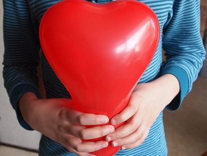 child holding red heart balloon