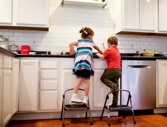 siblings standing on chairs doing the washing up