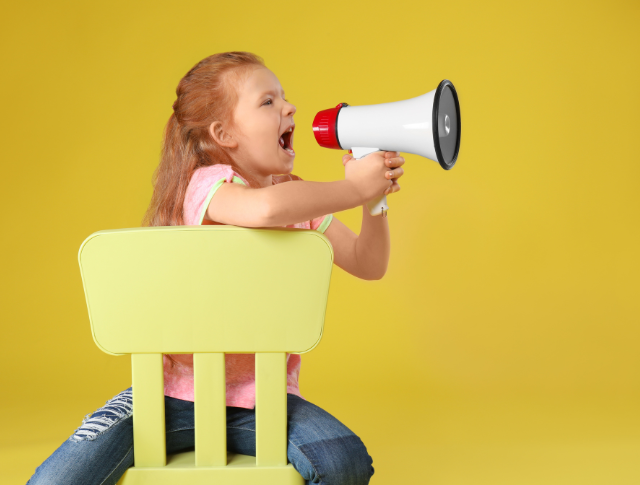 child sitting on chair yelling into megaphone