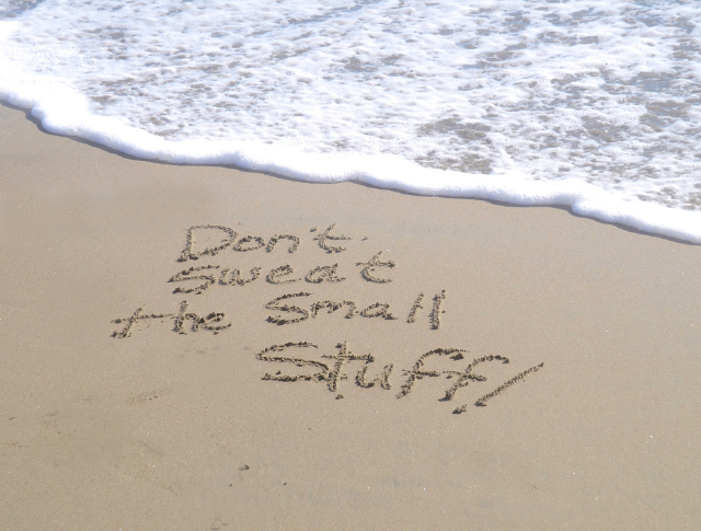 'Don't sweat the small stuff' written in the sand next to the sea