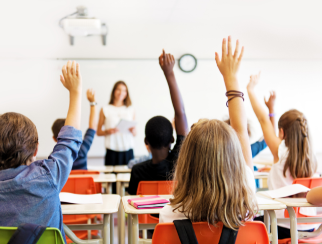 school kids in a classroom raising their hands