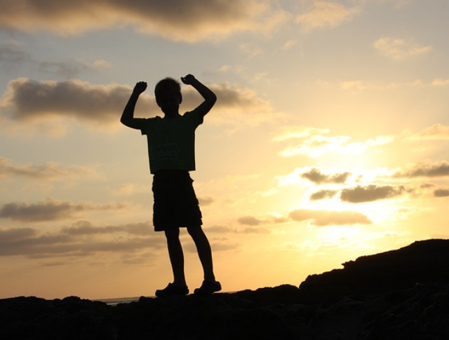 Boy on top of a hill with arms up in victory pose