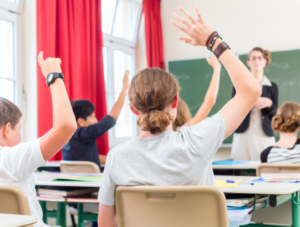 Secondary school children in classroom raising their hands